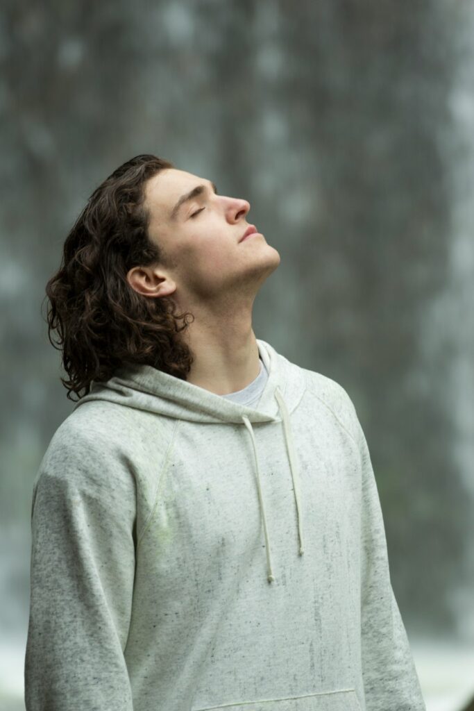 A person quietly sitting on a couch near a window, eyes closed, practicing mindful breathing in a calm living room.