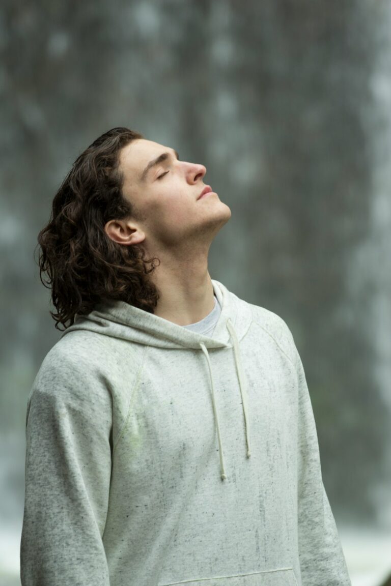 A person quietly sitting on a couch near a window, eyes closed, practicing mindful breathing in a calm living room.