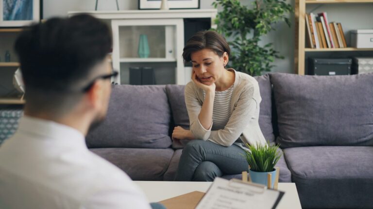 A person speaks with a counselor in a quiet room while holding a mug and sitting near a window.